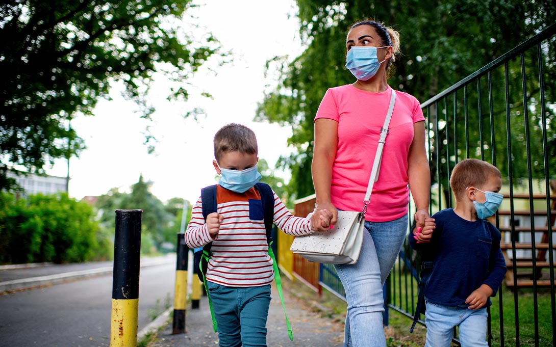 Parent walking two children to school with masks on