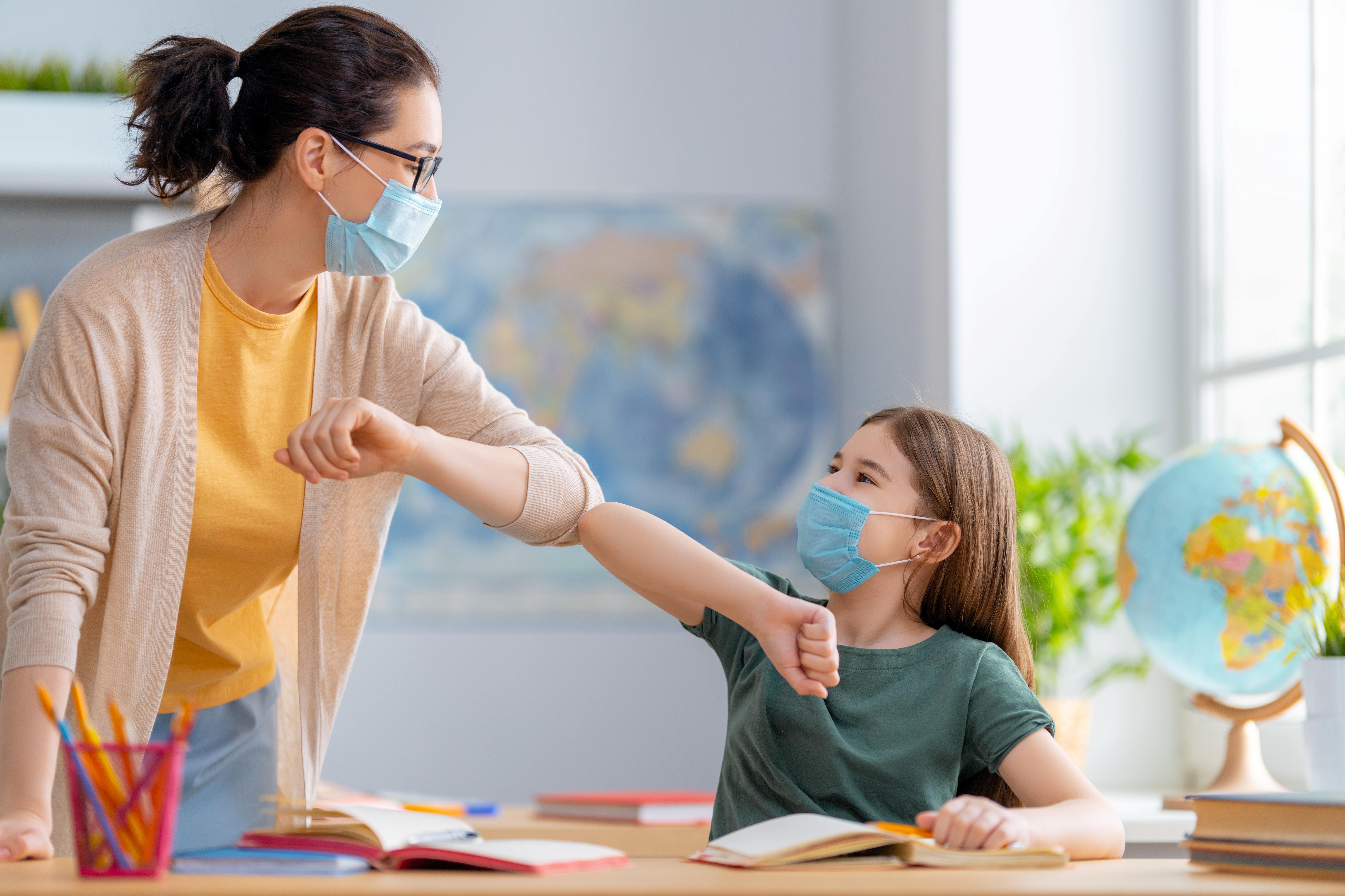 Teacher wearing a mask elbow bumping with child wearing a mask