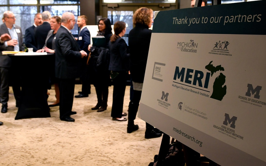 MERI (Michigan Education Research Institute) event poster with attendees in background